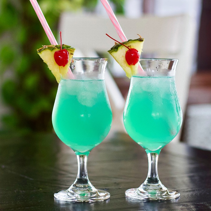 tropical rum punch in hurricane glasses, garnished with pineapple wedges and maraschino cherries.