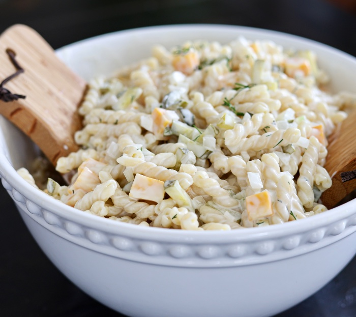 creamy dill pasta salad is a great side for many weeknight dinners. Here in a white bowl with wooden servers.