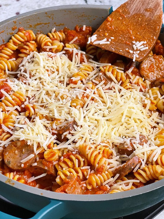 adding parmesan cheese to the sausage skillet dinner