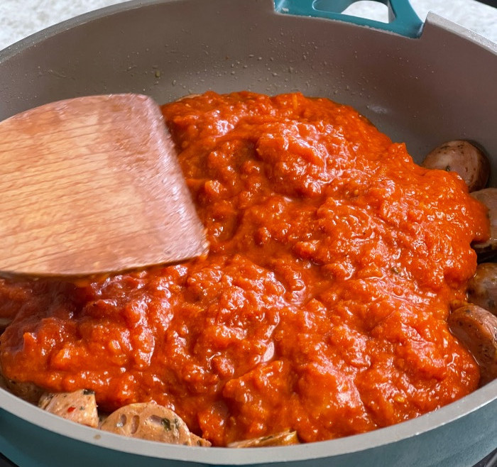 adding pasta sauce to pasta sausage dinner