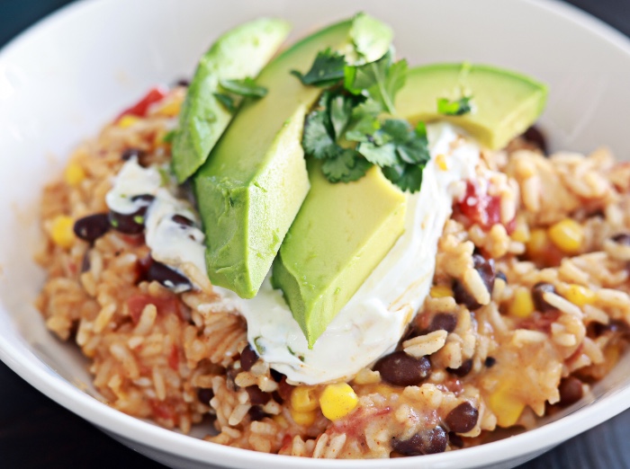 mexican chicken and rice in a white bowl with avocado slices on top