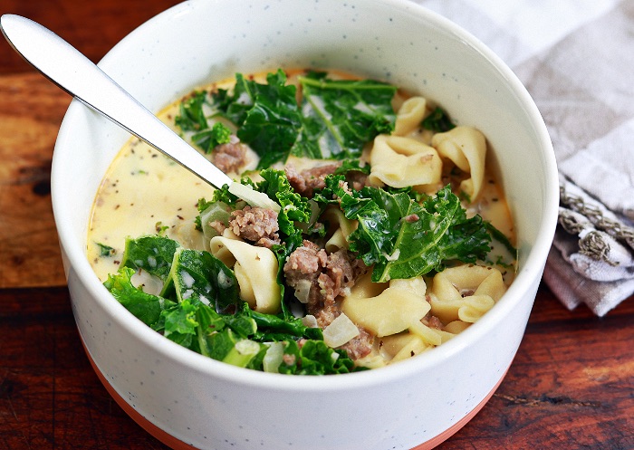 creamy tortellini soup in white bowl with spoon