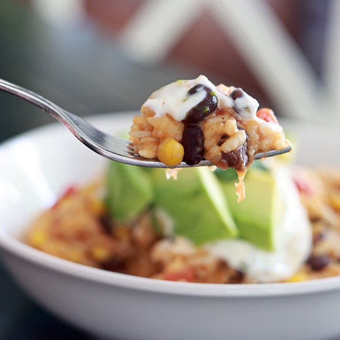 mexican chicken and rice in a white bowl with avocado slices on top. Forkful in foreground