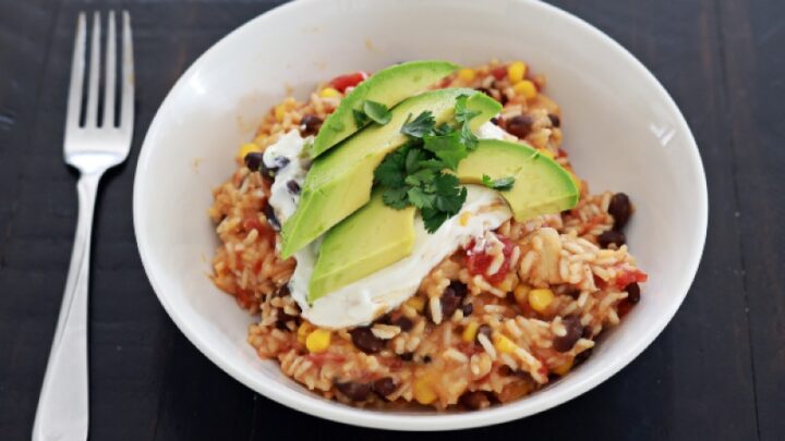 mexican chicken and rice in a white bowl with avocado slices on top