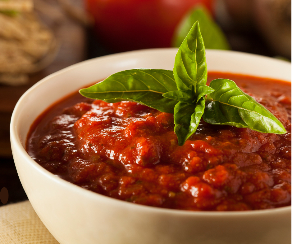 a bowl of red sauce with basil leaves