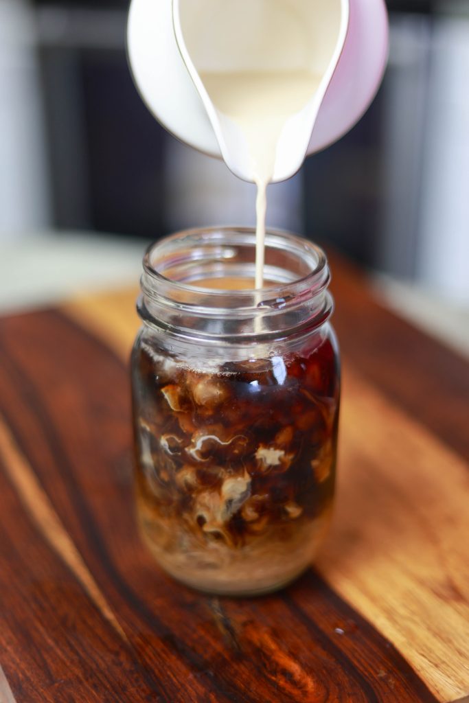 Pouring hazelnut coffee creamer into iced black coffee