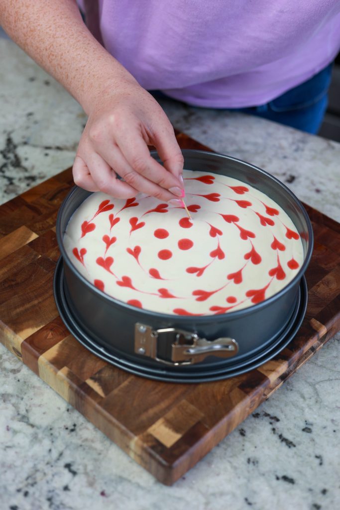 pulling a toothpick through strawberry swirl cheesecake