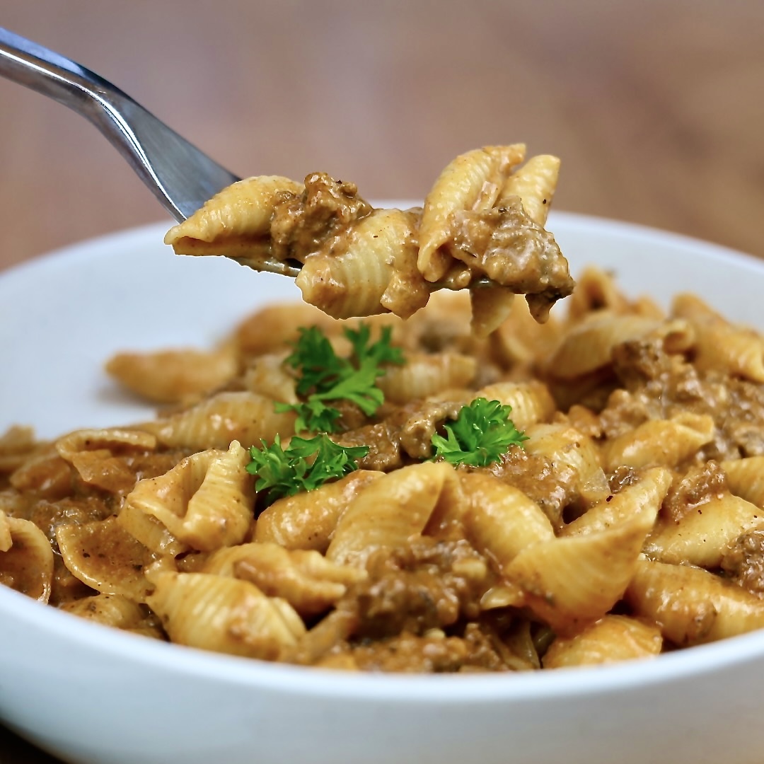 Cheesy beef and shells in a white bowl and on a fork for close up view