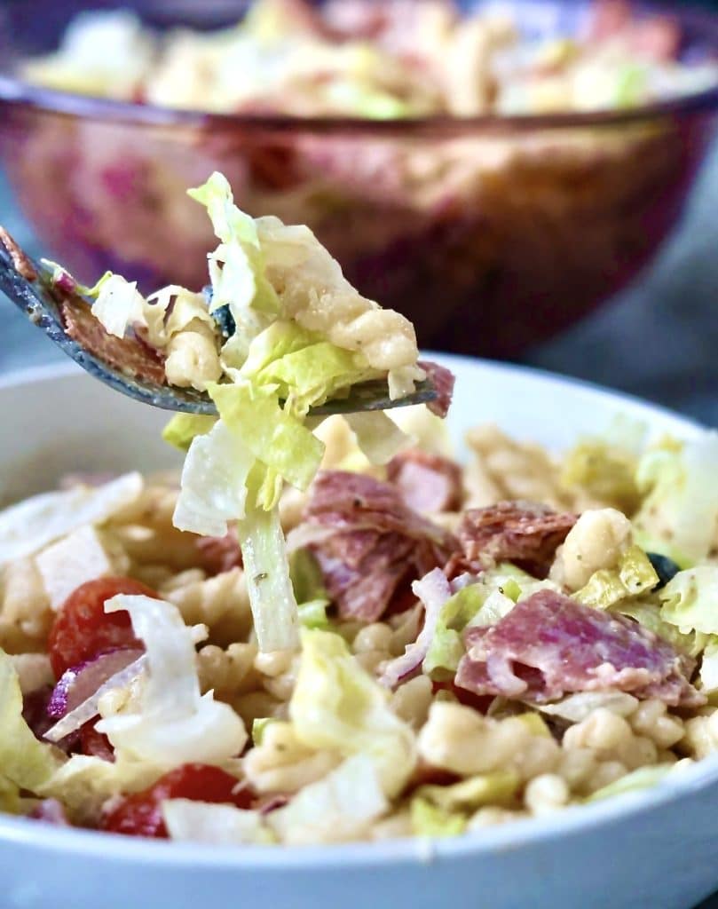 Italian Grinder Pasta Salad close up an oi fork ,over a bowl of salad