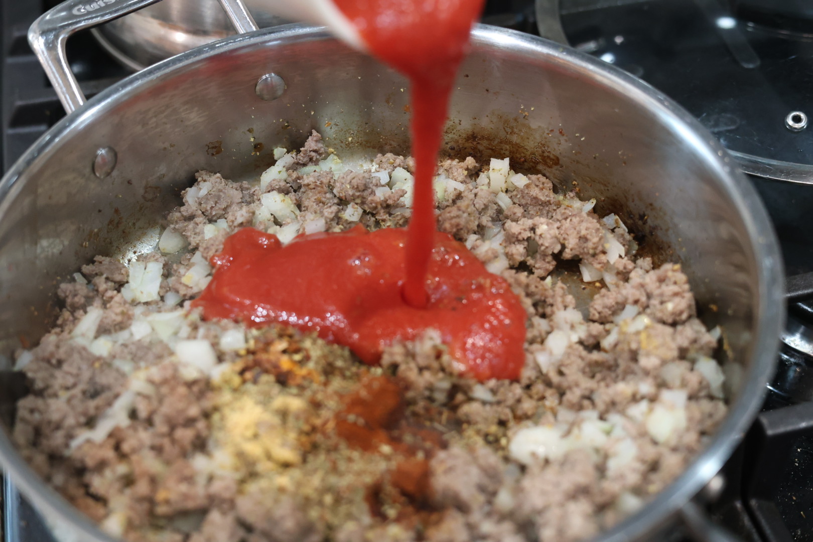 pouring in tomato sauce. cheesy beef and shells dinner in a skillet