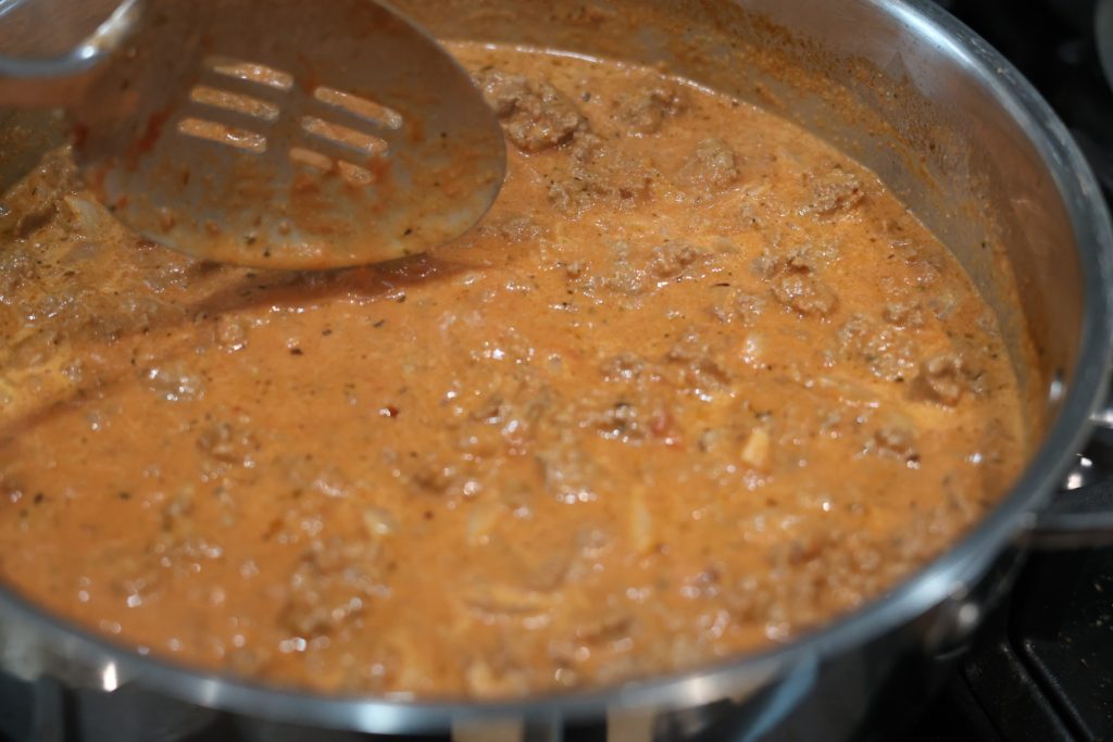 stirring sauce in a skillet for cheesy beef and shells