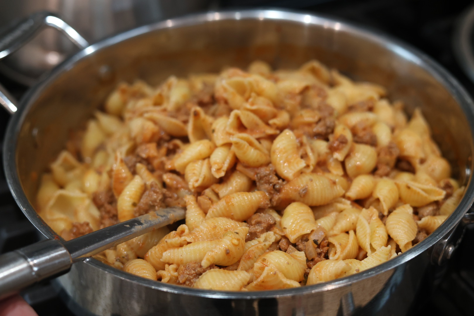 stirring cooked shell pasta into sauce for creamy beef and shells
