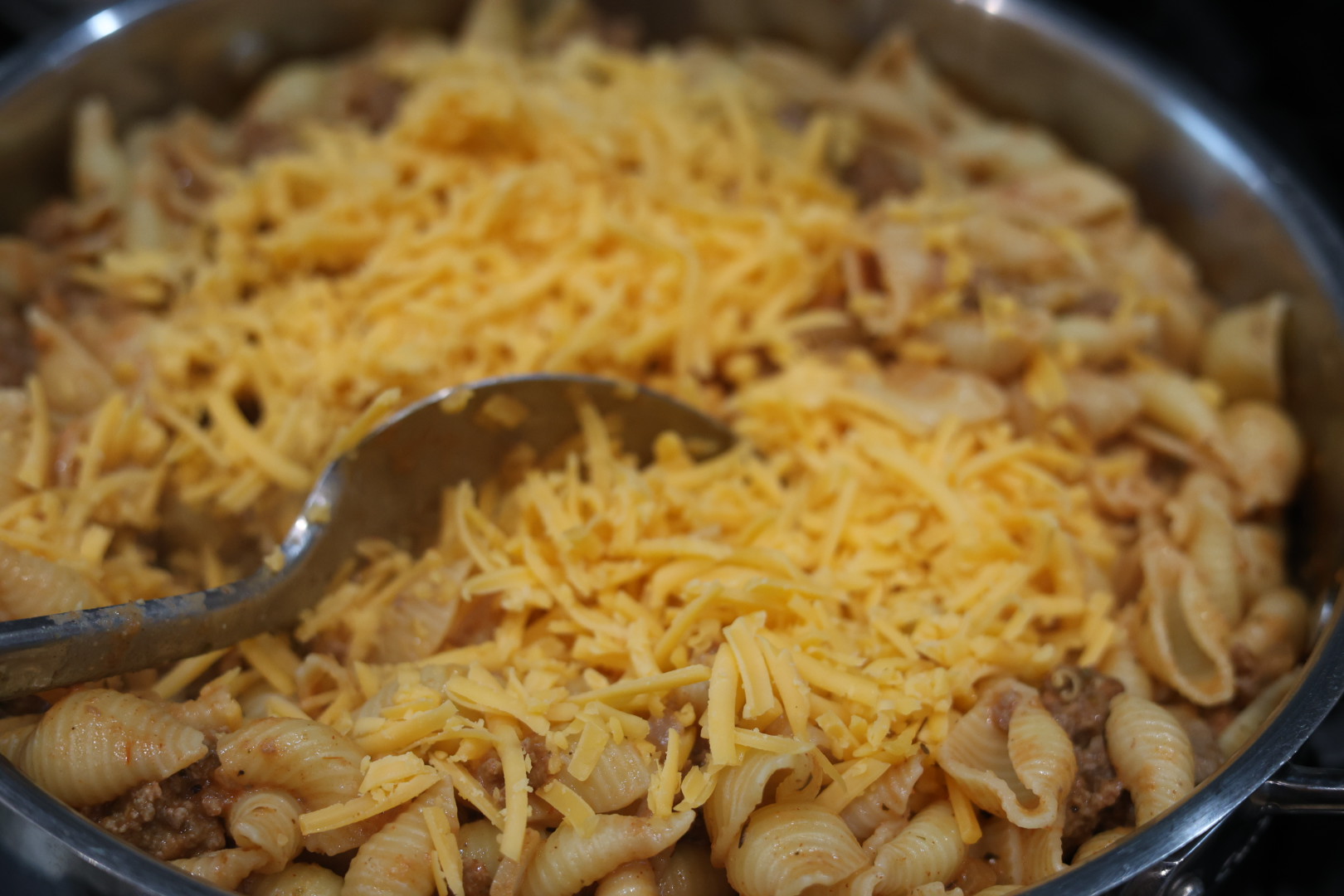 stirring grated cheese into cheesy beef and shells dinner