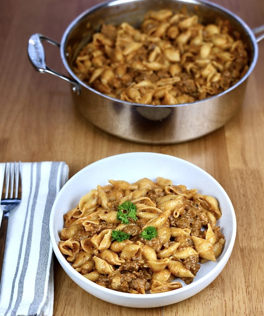 Cheesy Beef and Shells in a bowl with skillet in background.