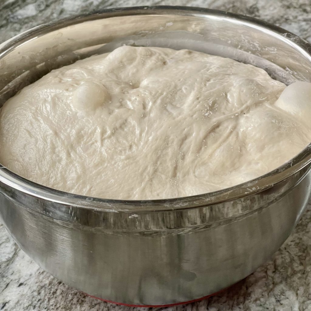 What Is Dough Structure in Sourdough? 11 Sourdough dough during bulk fermentation in a bowl, showing a puffy surface and fermentation bubbles.