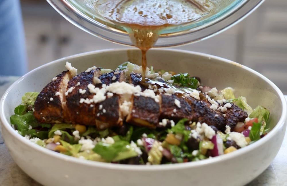 pouring honey lime dressing on blackened chicken salad
