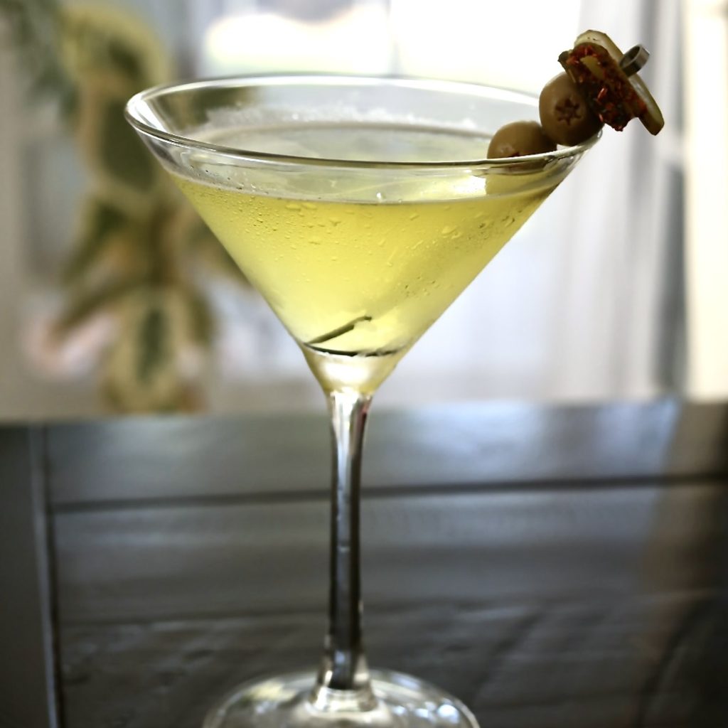 spicy Pickle-Tini in a chilled martini glass on a black table backlit by a window.